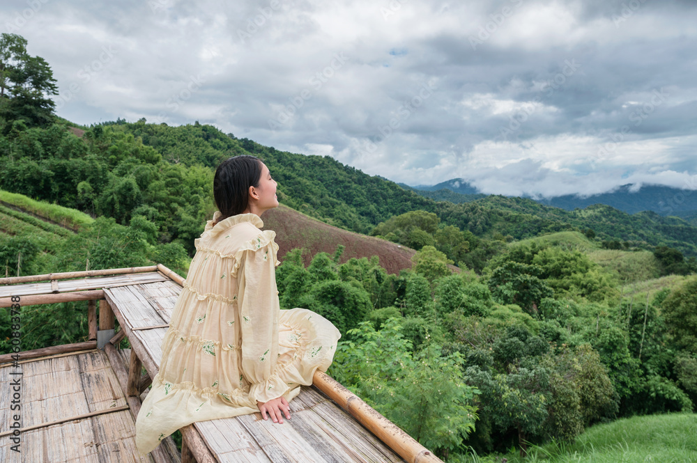 穿着黄色连衣裙的亚洲女人坐在山间的木制露台上度假