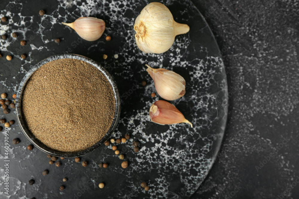 Bowl with black pepper powder and garlic on dark background