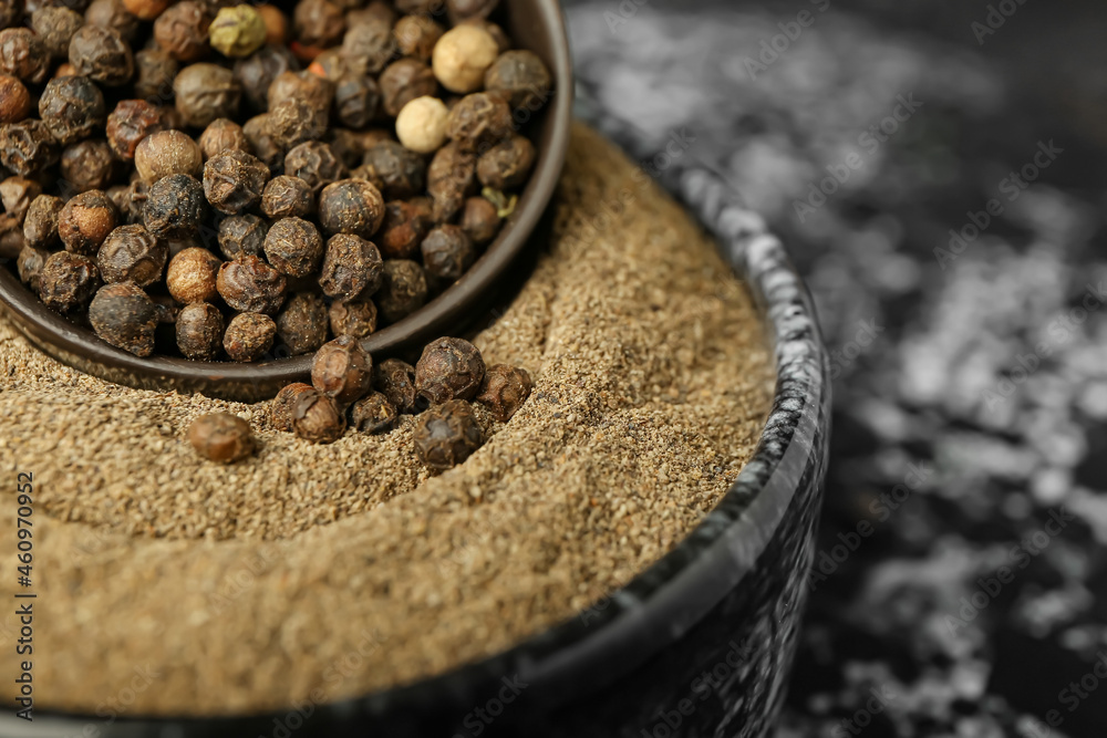 Bowls with black peppercorns and powder on dark background, closeup