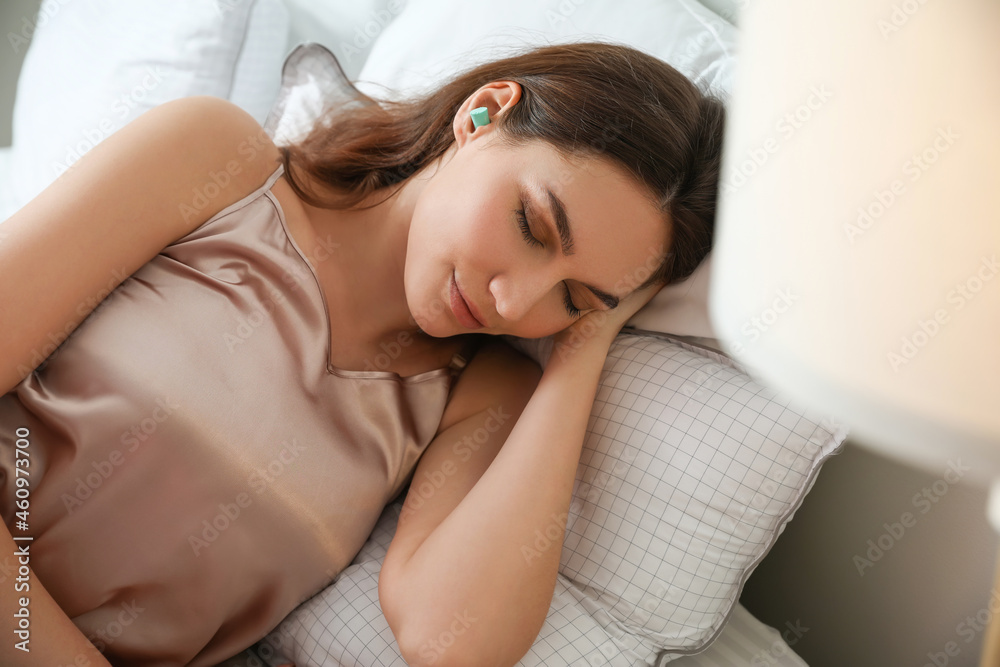 Beautiful young woman with ear plugs sleeping in bed