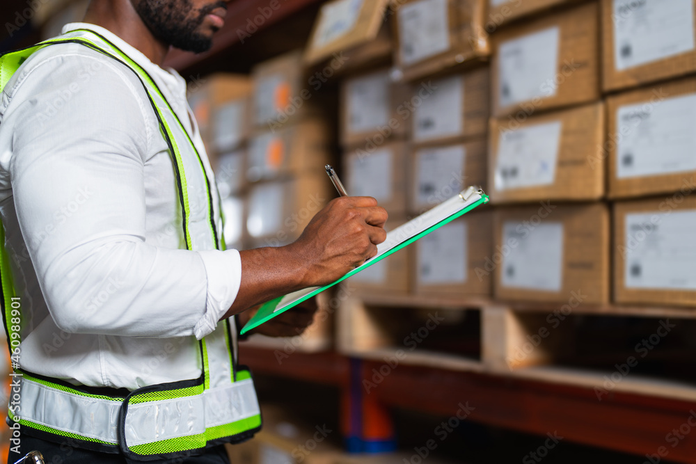 Portrait of an African warehouse manager holding a clipboard checking inventory in a large distribut