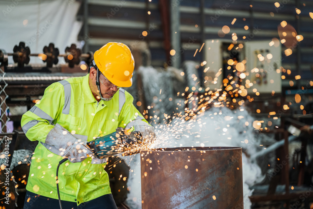 Industrial worker is working electric wheel grinding on steel structure in factory.