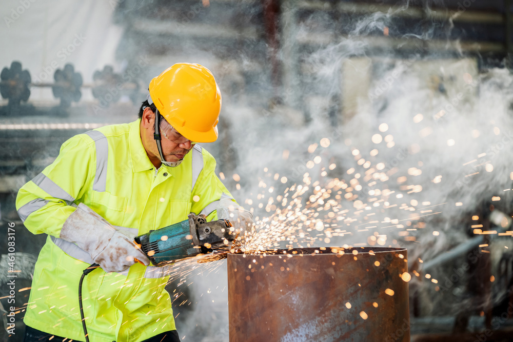 Asian worker is working electric wheel grinding on steel structure in factory.