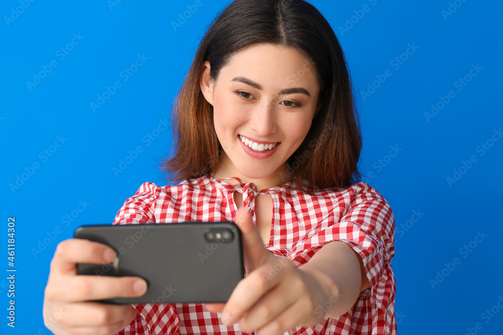 Stylish young Asian woman taking selfie on color background