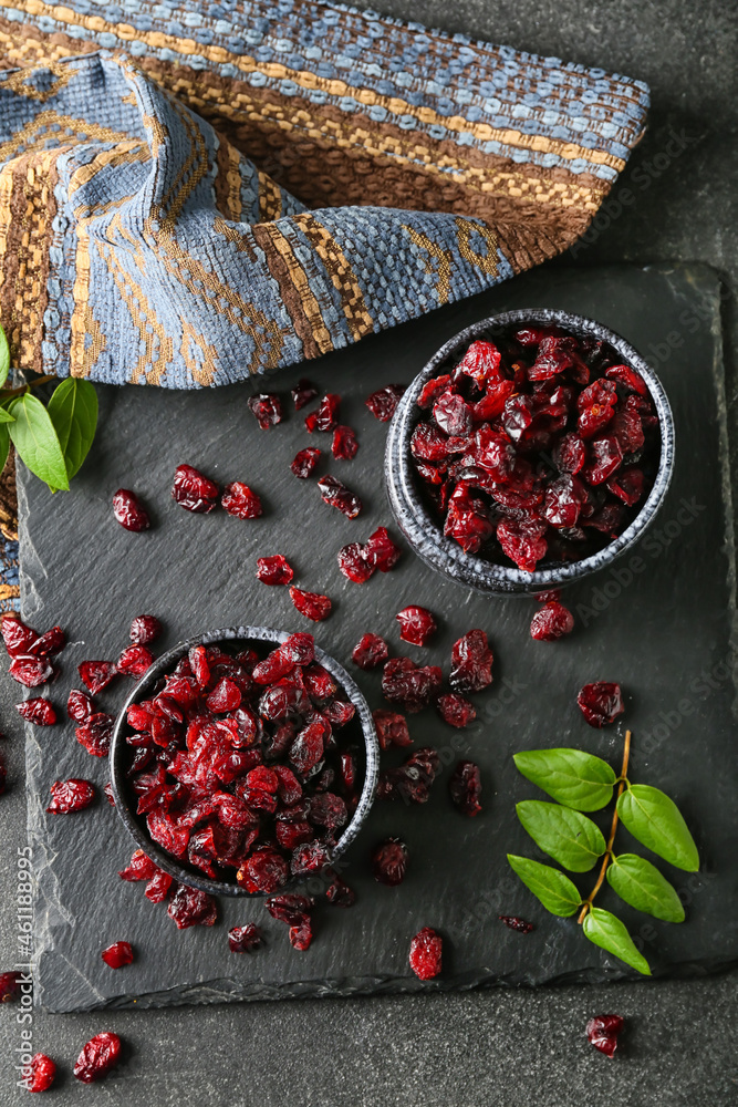 Bowls with tasty dried cranberries on dark background