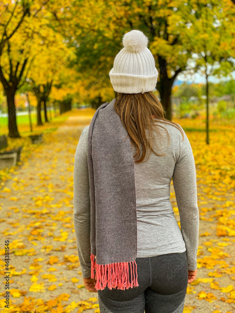 CLOSE UP: Unrecognizable woman strolls along a scenic autumn colored avenue.