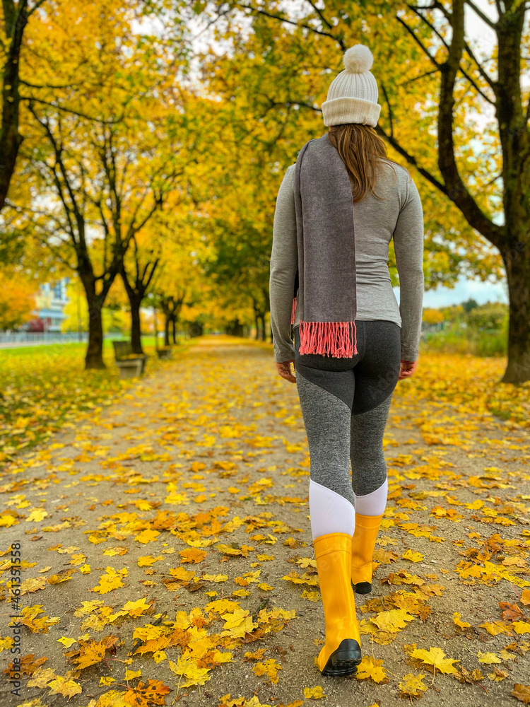 VERTICAL: Unrecognizable woman strolls along a scenic autumn colored avenue.