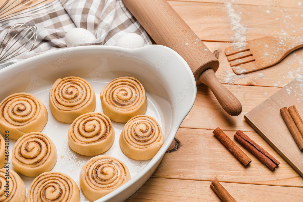 Baking dish with uncooked cinnamon rolls on wooden background