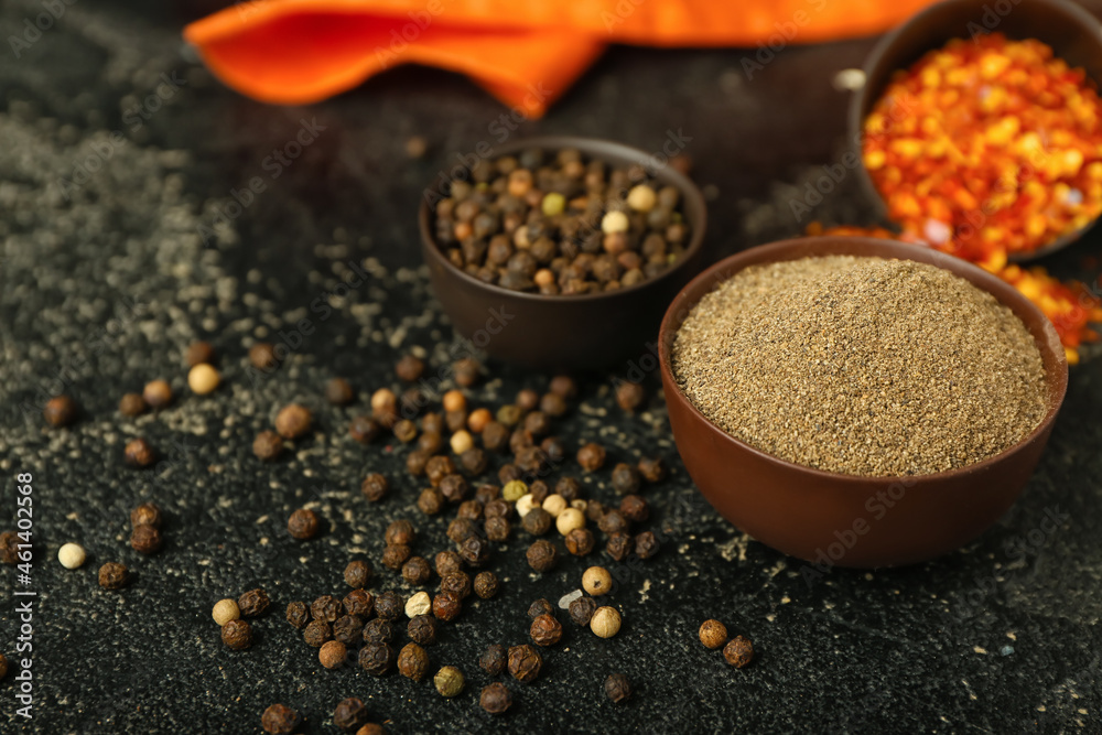 Bowls with black pepper powder and peppercorns on dark background