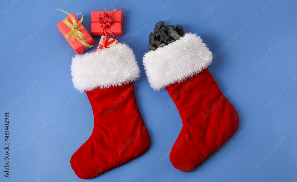 Christmas socks with coal and gift boxes on color background