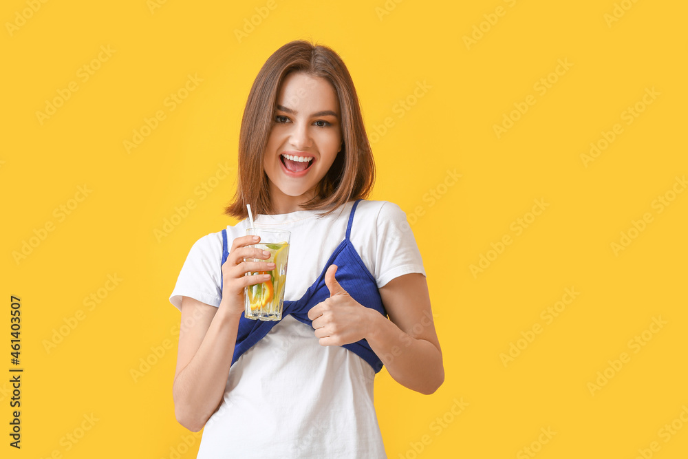 Beautiful young woman with fresh lemonade showing thumb-up on color background