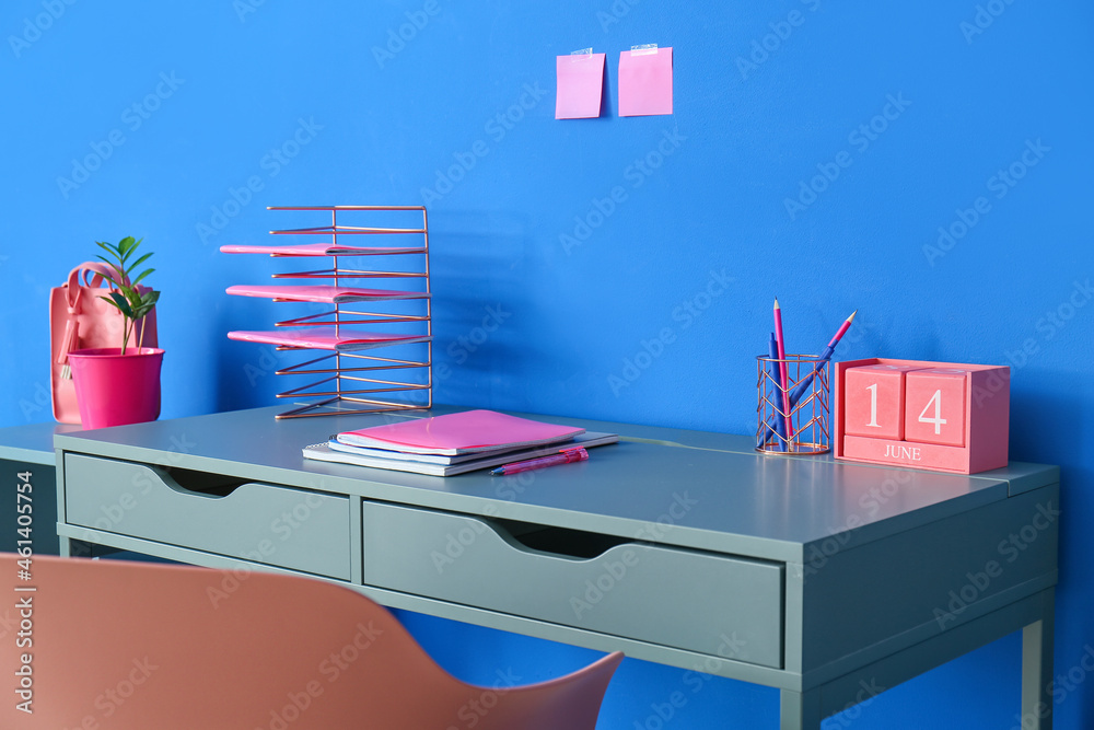 Modern desk with stationery near blue wall