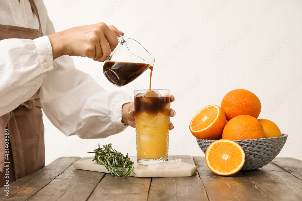 Woman pouring coffee into glass with orange juice on light background, closeup