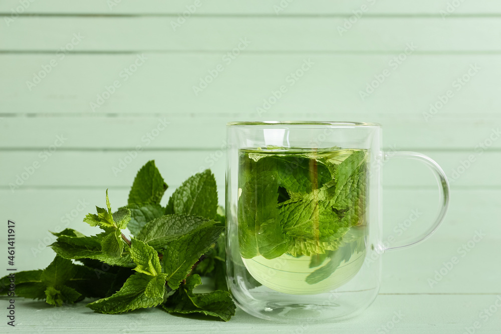 Glass cup of tasty mint tea on green wooden background