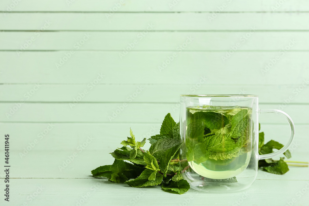 Glass cup of tasty mint tea on green wooden background