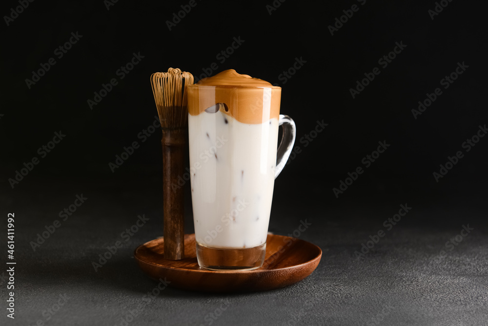 Glass cup of tasty dalgona hojicha latte and chasen on dark background