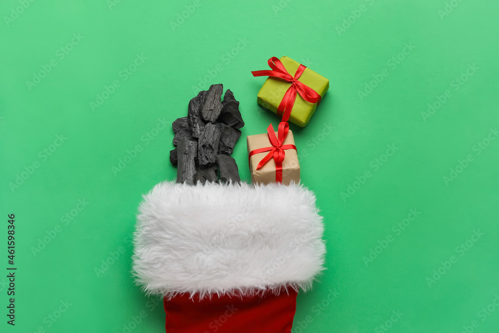 Christmas sock with coal and gift boxes on color background