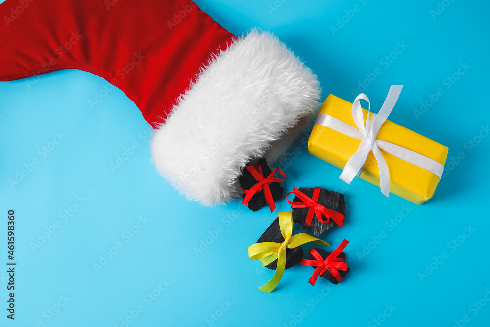 Christmas sock with coal and gift on color background