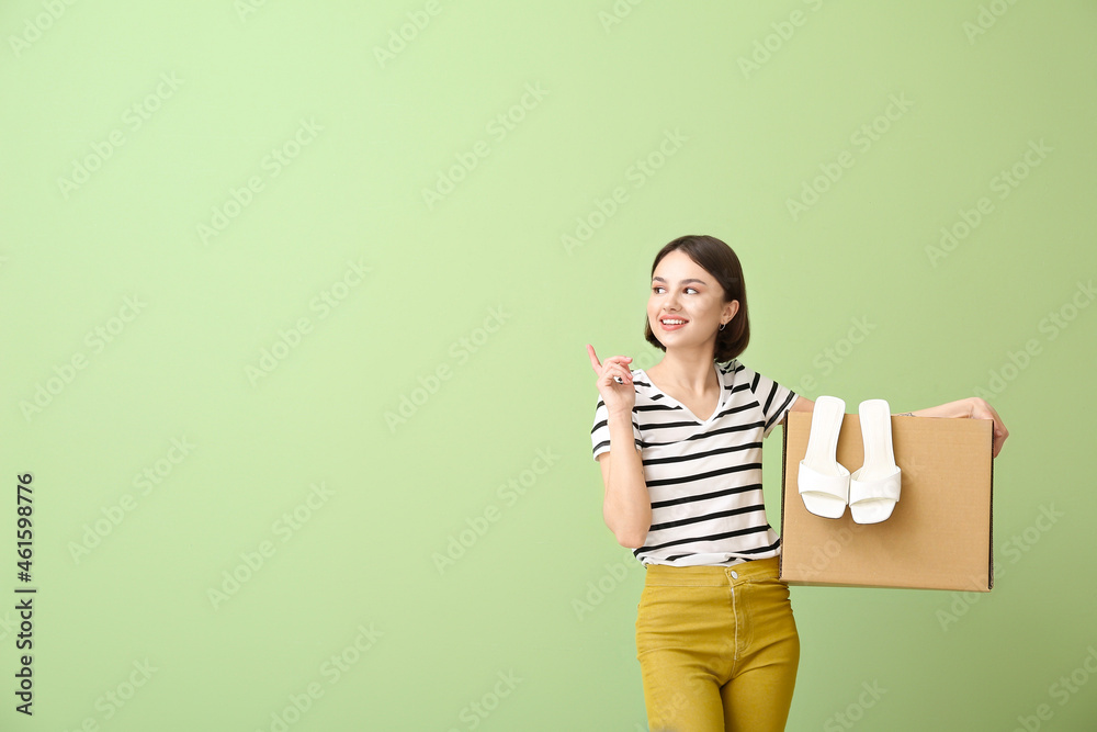 Young woman with wardrobe box pointing at something on color background