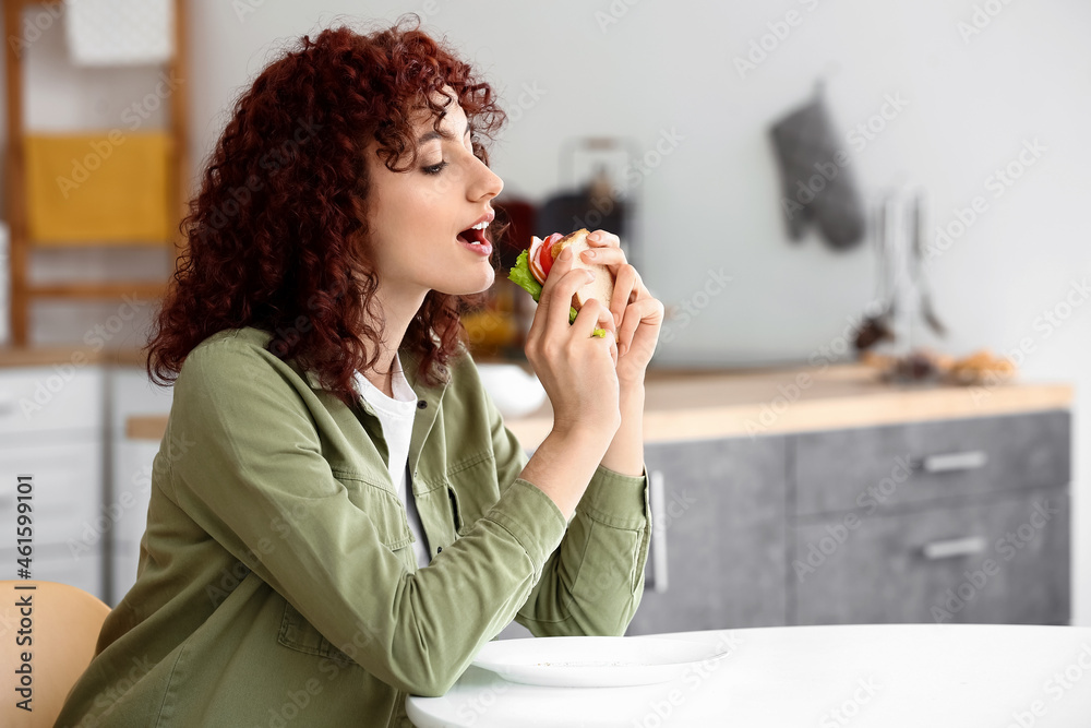 漂亮的年轻女人在厨房的桌子上吃美味的三明治