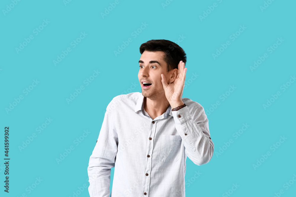 Young gossip man trying to hear something on blue background