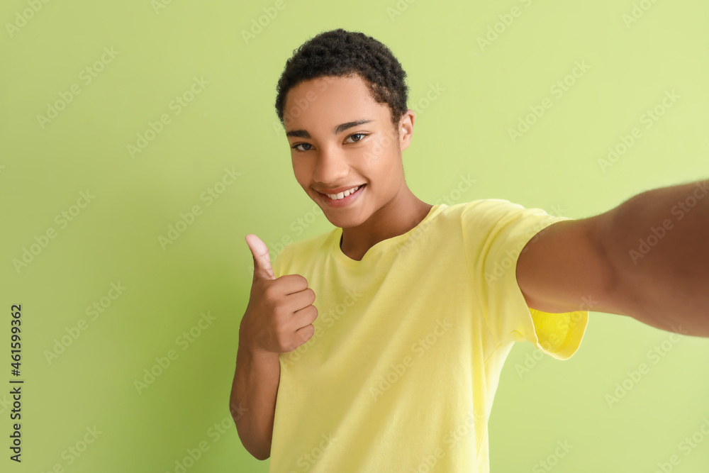 Happy African-American teenage boy taking selfie on color background