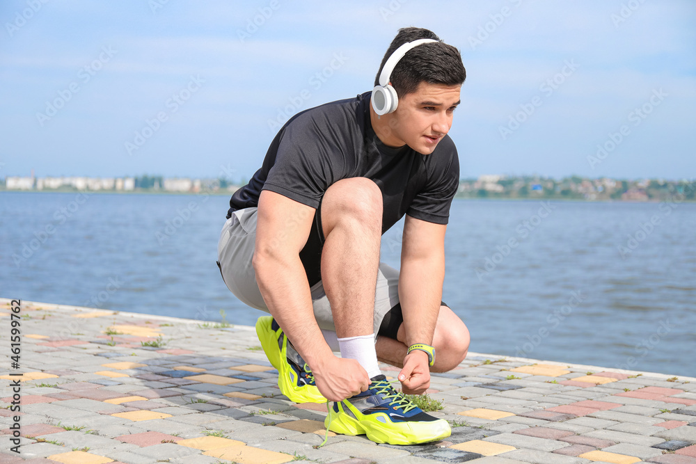 Muscular young man tying shoe lace near river