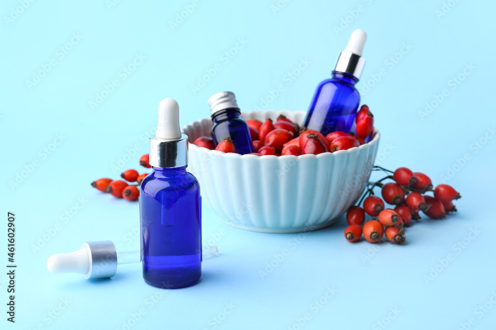 Bottles of essential oil and ripe rose hip berries on color background