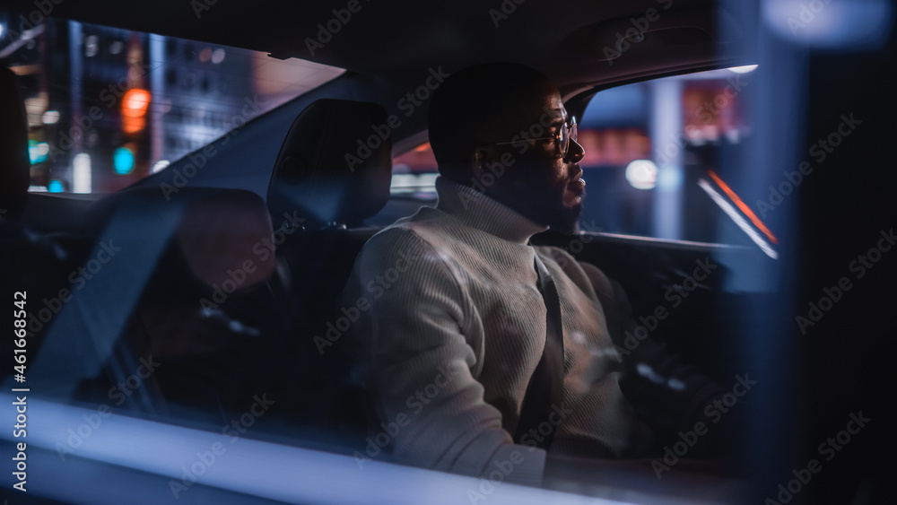 Stylish Black Man in Glasses is Commuting Home in a Backseat of a Taxi at Night. Handsome Male Passe