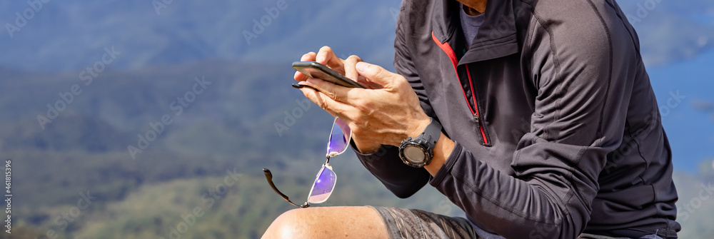 山の頂上でスマートフォンを操作する男性