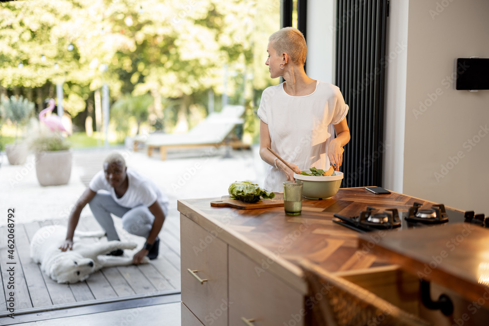 Black man caress dog while his european girlfriend looking on it and holding bowl with salad. Concep