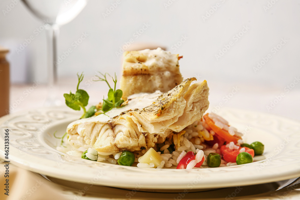 Plate with tasty baked cod fillet, rice and vegetables on table in restaurant, closeup