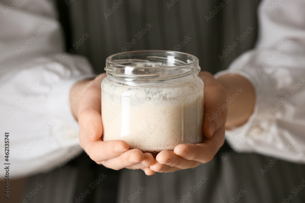 Woman holding glass jar of fresh sourdough, closeup