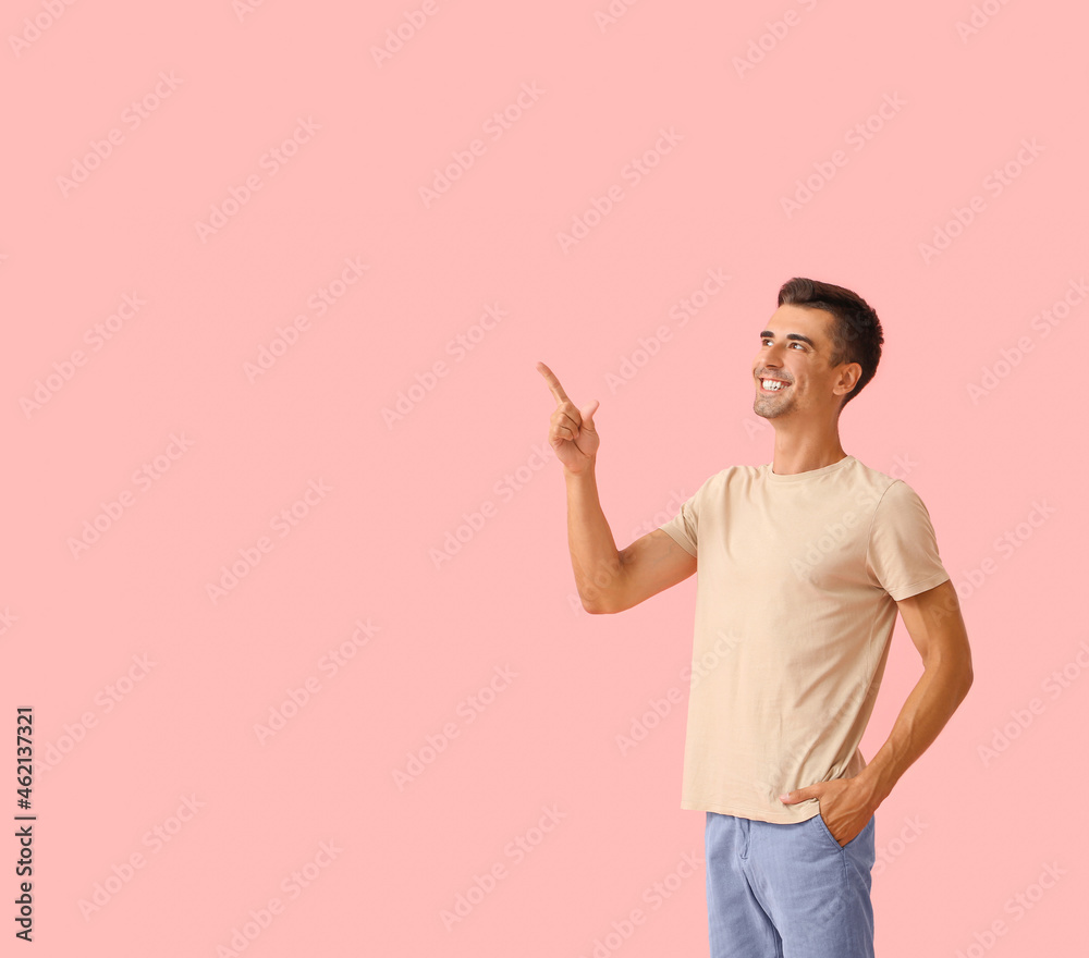 Handsome young man in stylish t-shirt pointing at something on color background