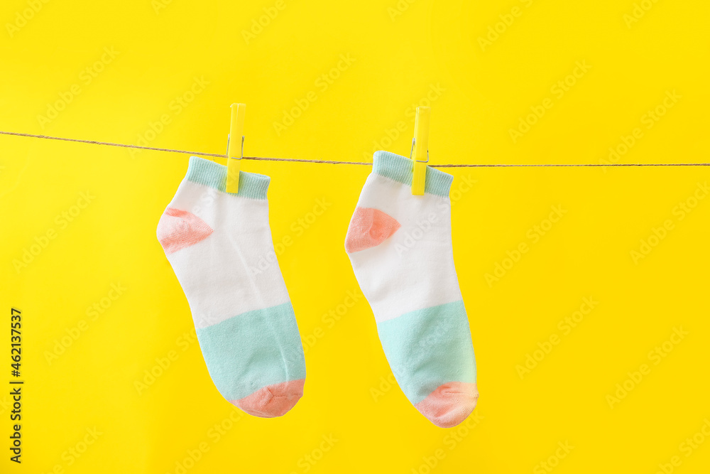 New socks hanging on rope against yellow background