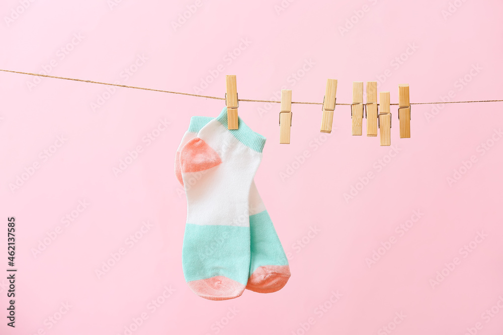 Pair of socks and clothespins hanging on rope against pink background