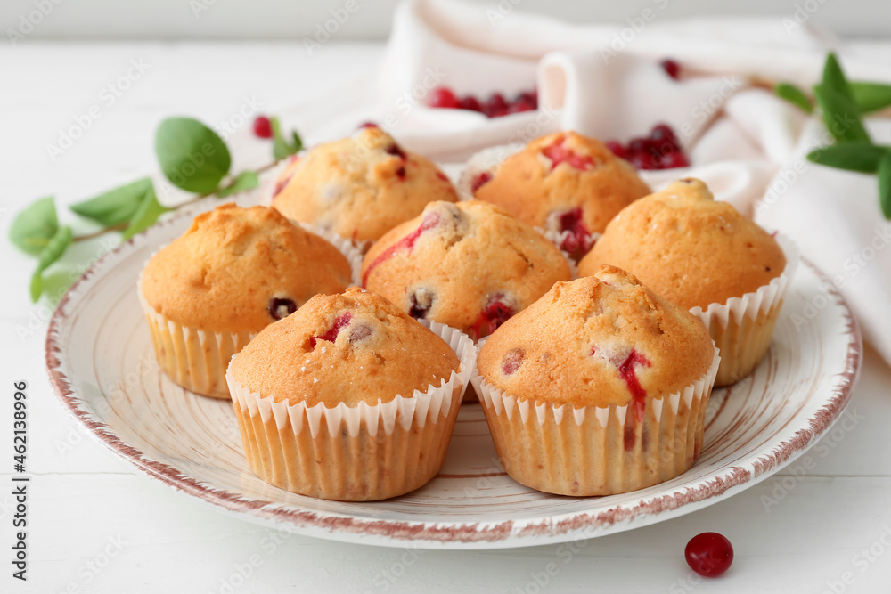 Plate with tasty cranberry muffins on light wooden background