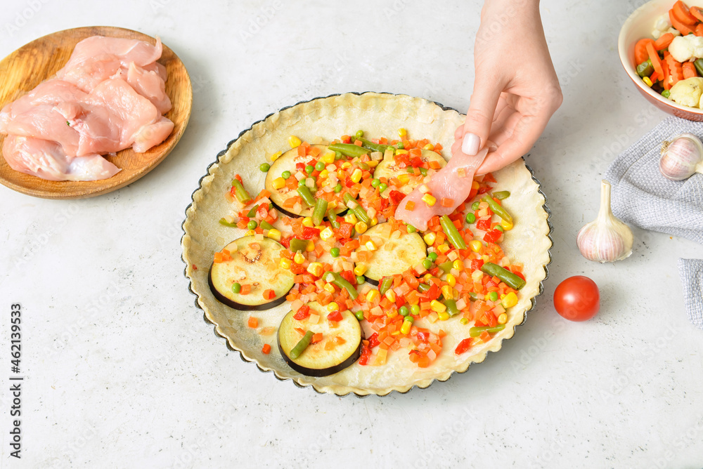 Woman preparing chicken pot pie with vegetables on white background