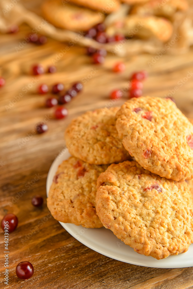 Plate with tasty cranberry cookies on wooden background, closeup