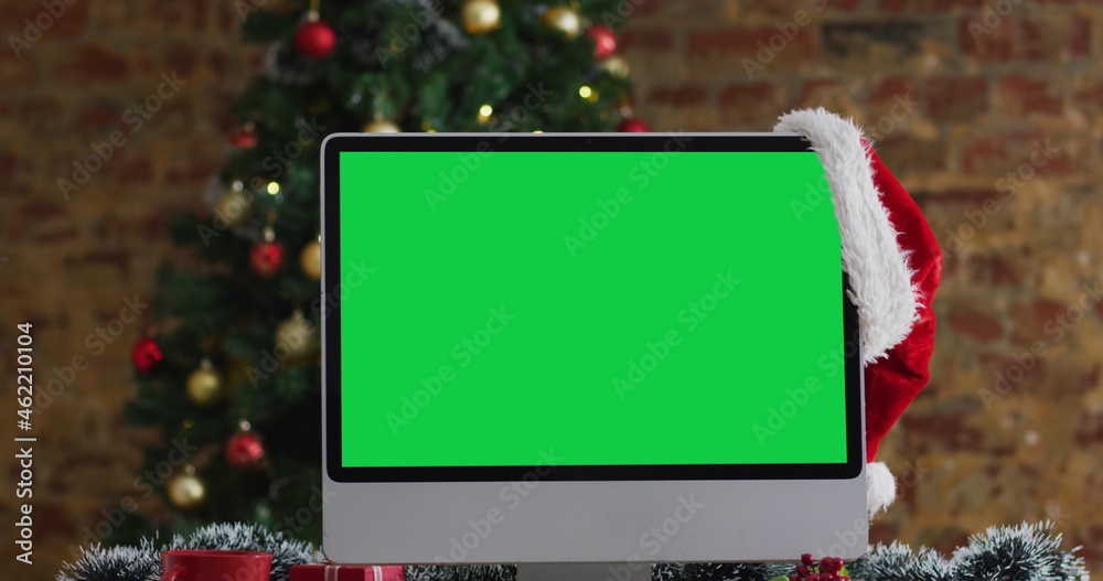 Santa hat hanging on computer monitor with copy space, with christmas decorations and tree