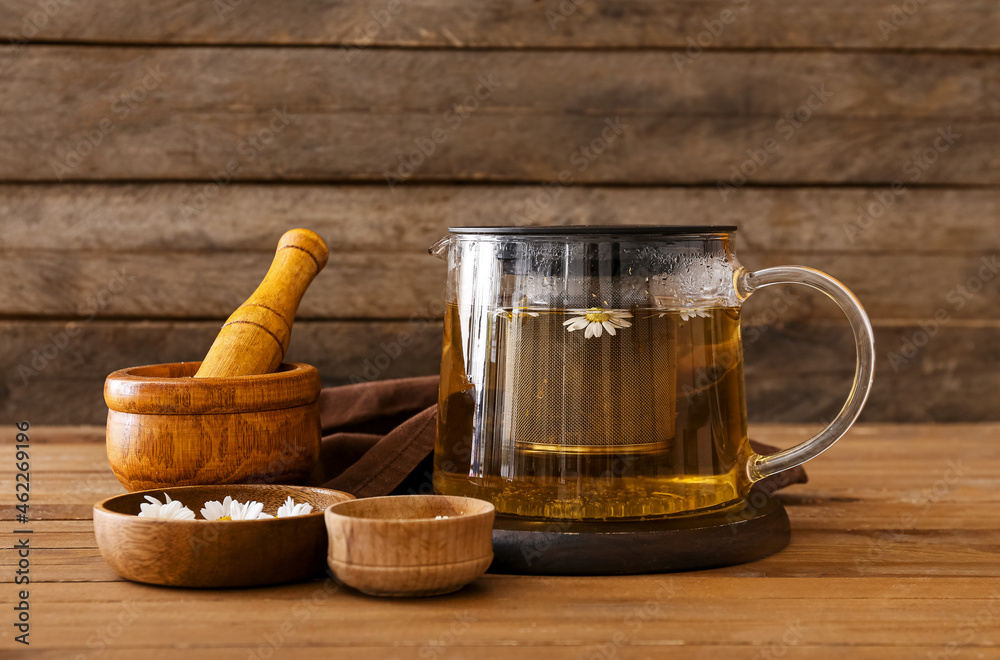 Teapot of tasty chamomile tea and flowers on wooden table