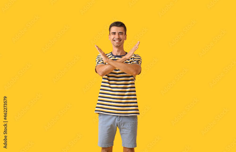 Handsome young man in stylish t-shirt showing STOP gesture on color background