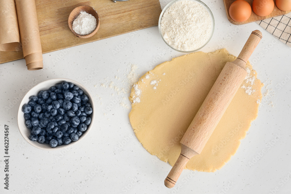 Raw dough with ingredients for blueberry galette on light background