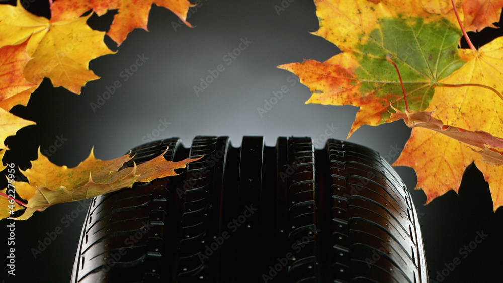 Car tire with falling autumn leaves.