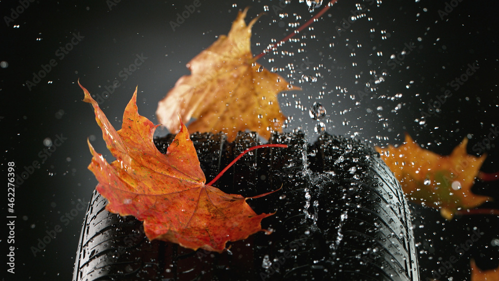 Car tire with falling autumn leaves and splashing water