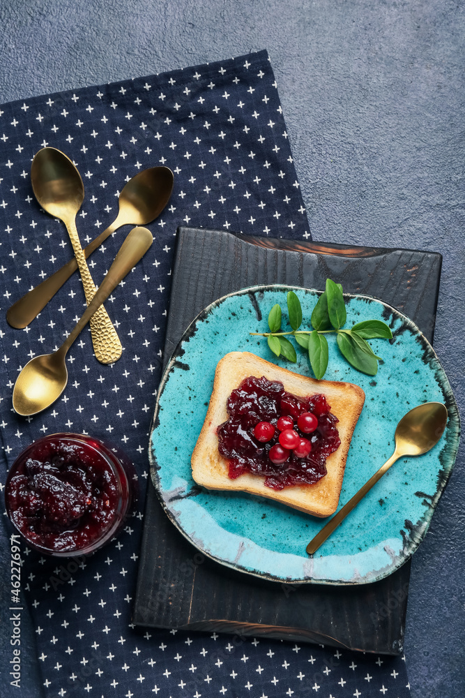 Plate with toast and tasty cranberry jam on dark background