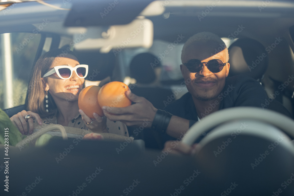 Multiracial couple riding together in car. Young european woman holding organic groceries after shop