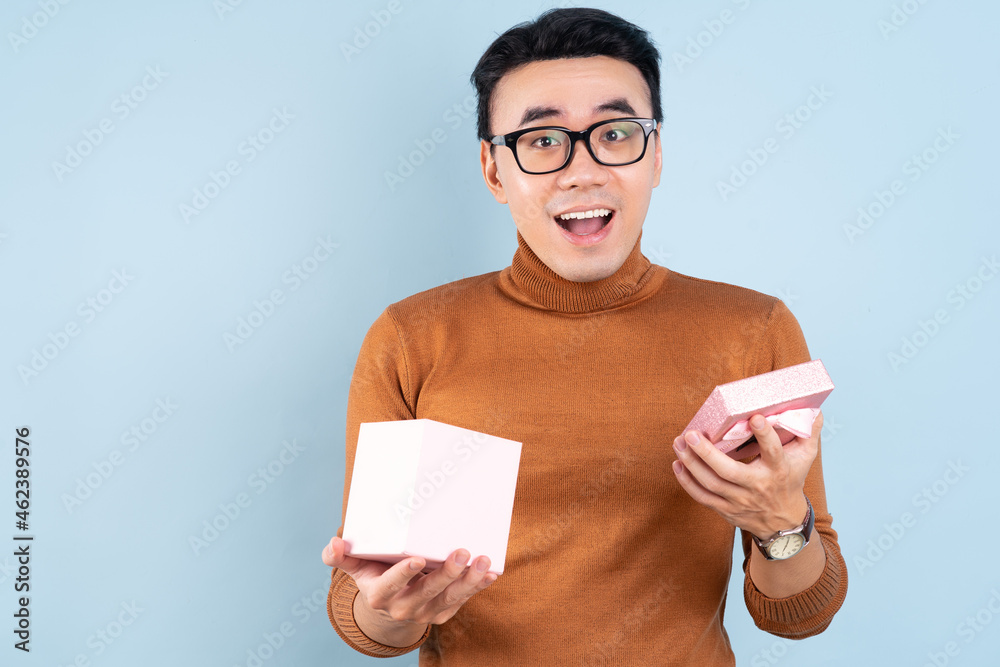 Asian man holding pink giftbox on blue background