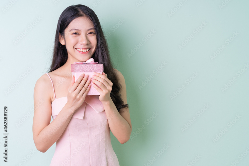 Beautiful young Asian woman holding pink gift box on green background