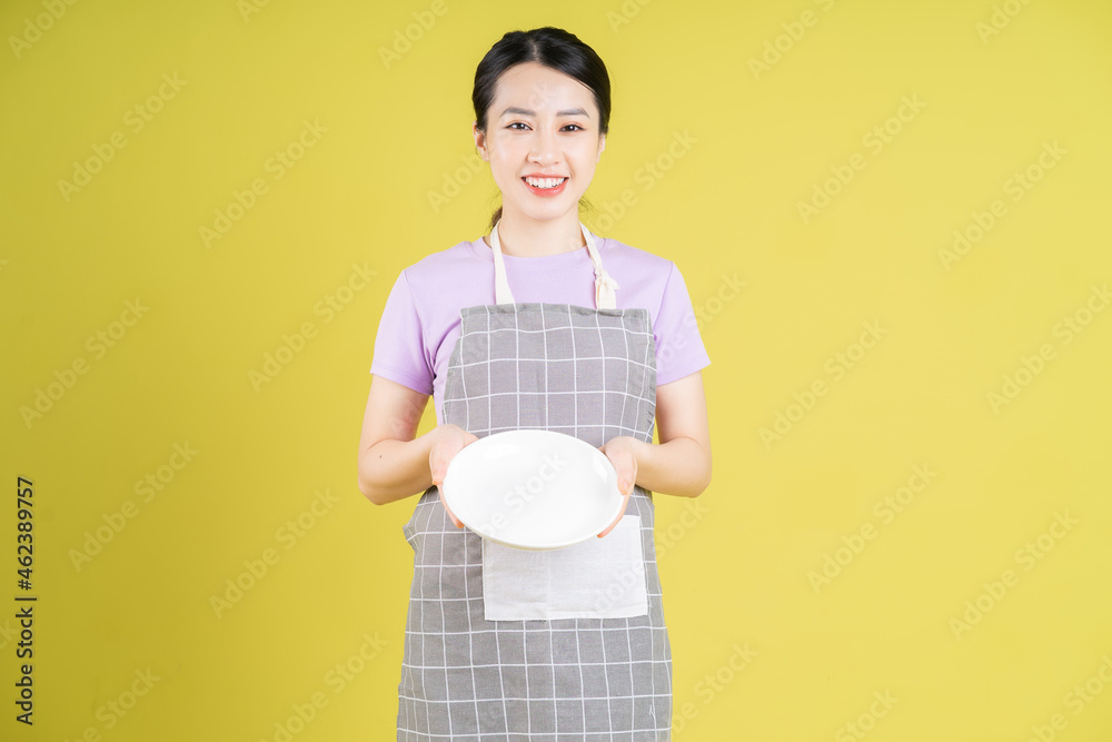 Young Asian housewife posing on yellow background